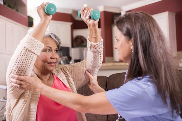 Home healthcare nurse helping senior woman with physical therapy.
