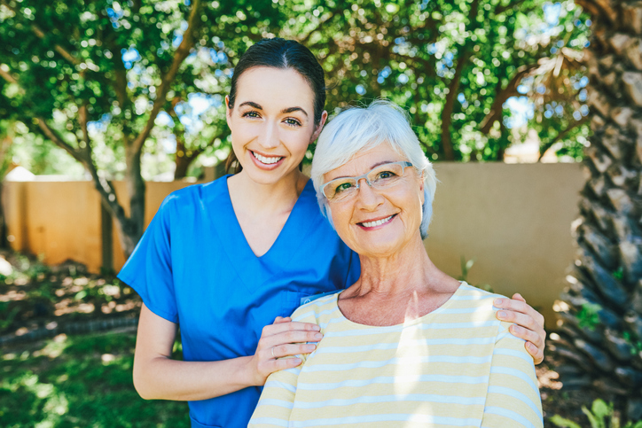 Senior woman standing by the side of her caregiver and smiling.